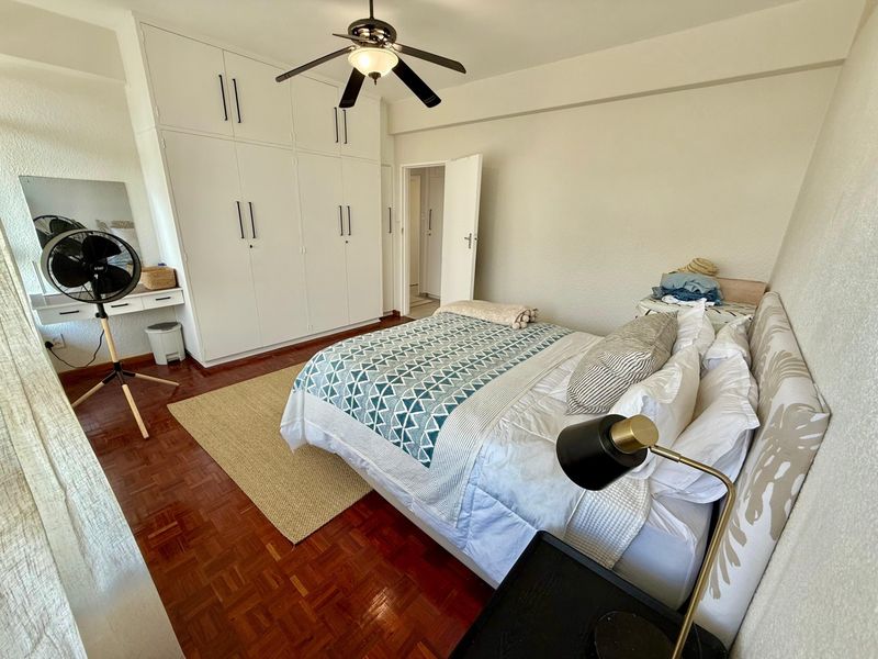 A well-maintained bedroom featuring classic parquet flooring, ample built-in cupboard storage, and a central ceiling fan.