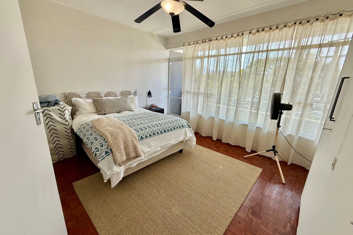 A bright bedroom featuring classic parquet flooring, a ceiling fan, and large windows that provide ample natural light.