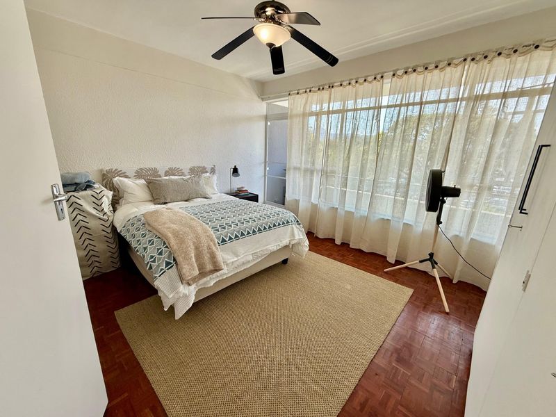 A bright bedroom featuring classic parquet flooring, a ceiling fan, and large windows that provide ample natural light.
