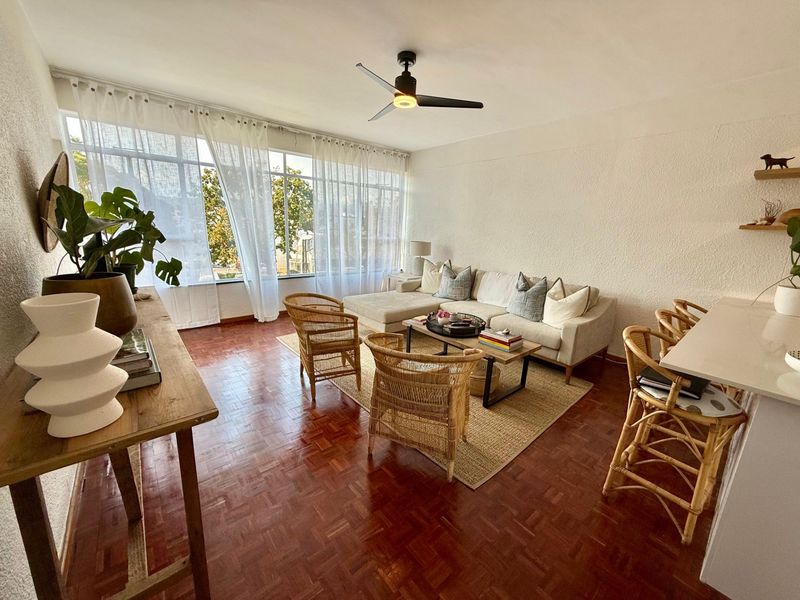 Bright and spacious living room featuring classic parquet flooring, a modern ceiling fan, and large windows that provide ample natural light.