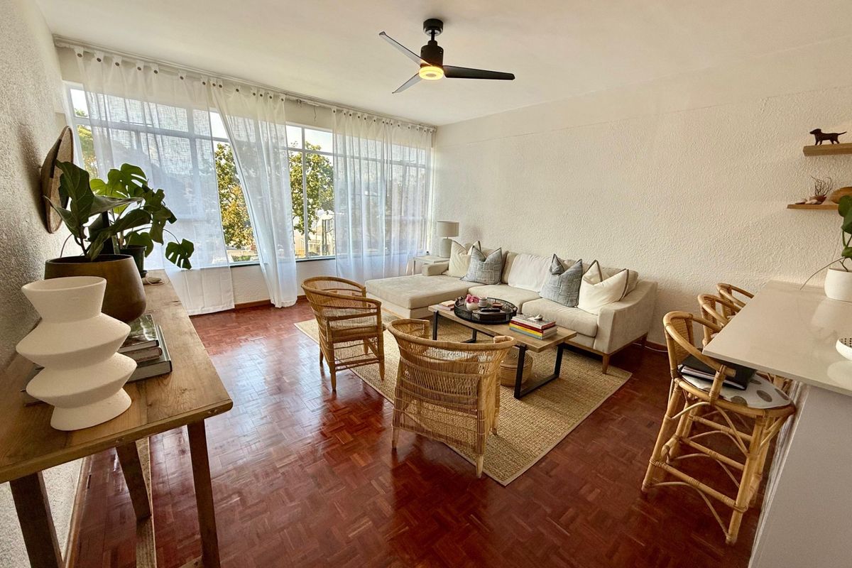 Bright and spacious living room featuring classic parquet flooring, a modern ceiling fan, and large windows that provide ample natural light.