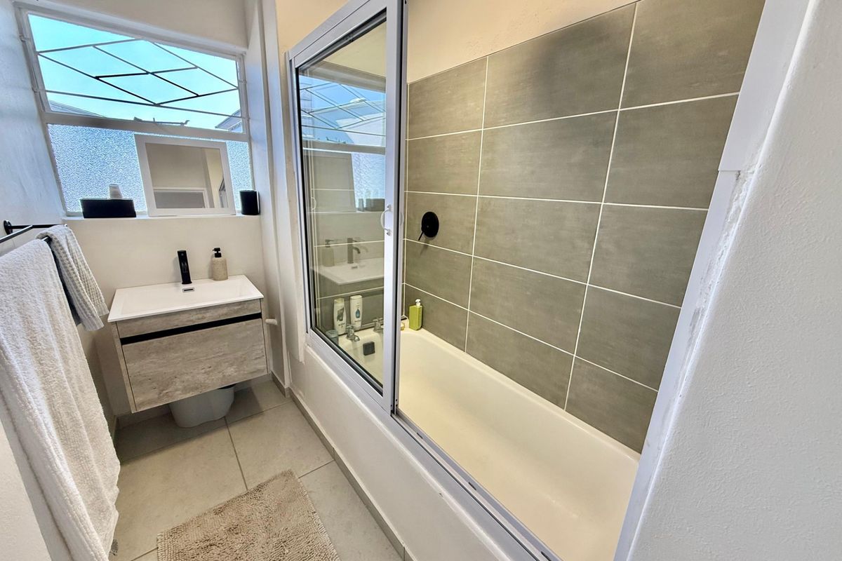 Modern bathroom featuring a vanity with basin, a bathtub with a sliding glass screen, and neutral wall and floor tiling.