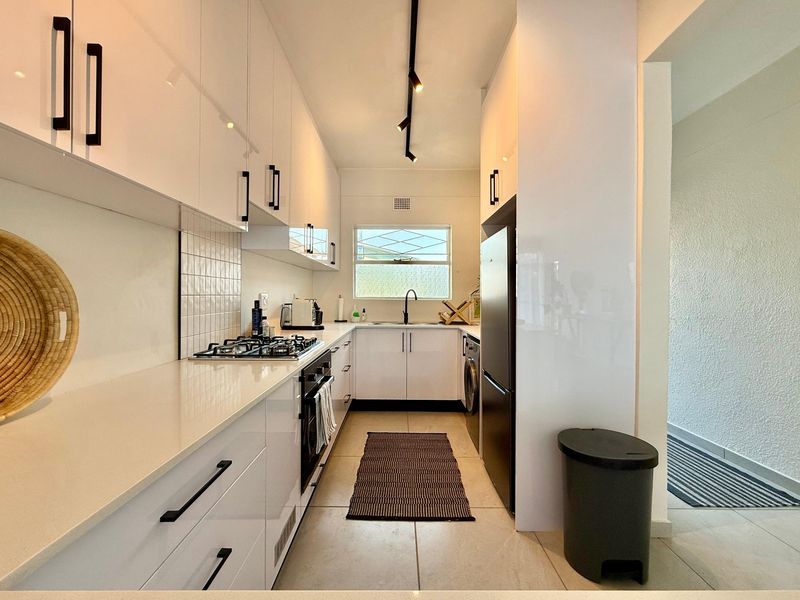 Modern galley-style kitchen featuring white high-gloss cabinetry, quartz countertops, gas hob, built-in oven, and contemporary track lighting.