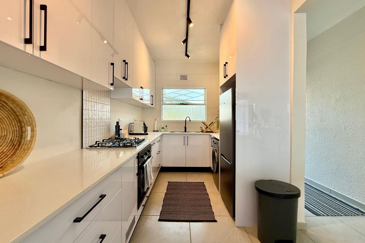 Modern galley-style kitchen featuring white high-gloss cabinetry, quartz countertops, gas hob, built-in oven, and contemporary track lighting.
