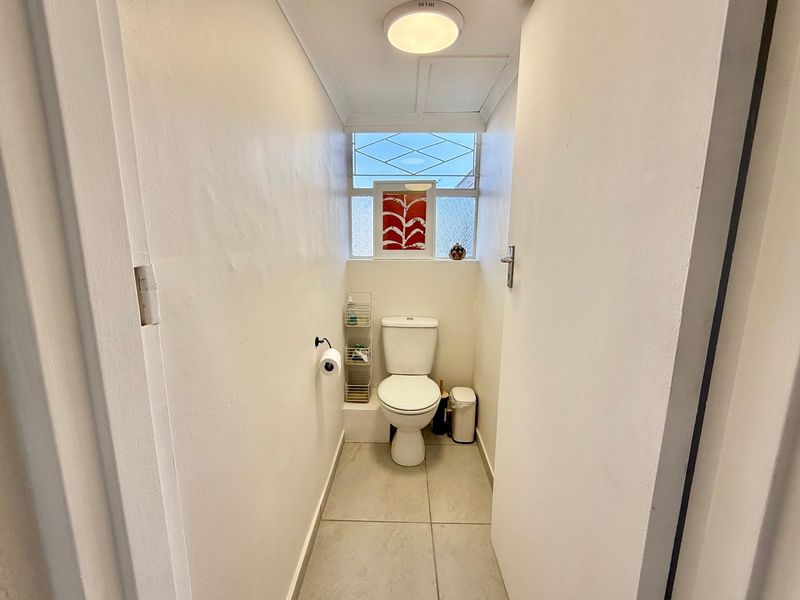 A compact guest bathroom featuring a standard toilet, tiled flooring, and a frosted glass window for natural light.