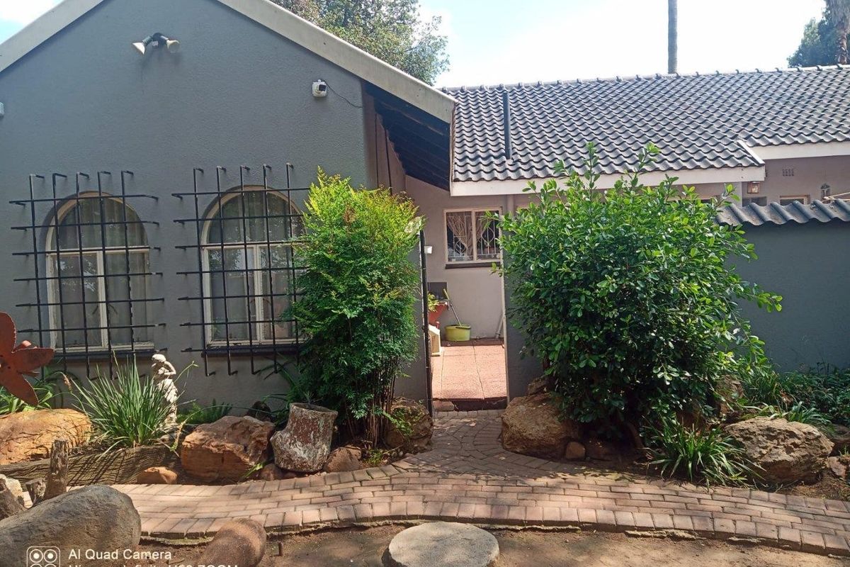 Rear exterior view of the house featuring a paved walkway, landscaped garden area, and security bars on the windows.