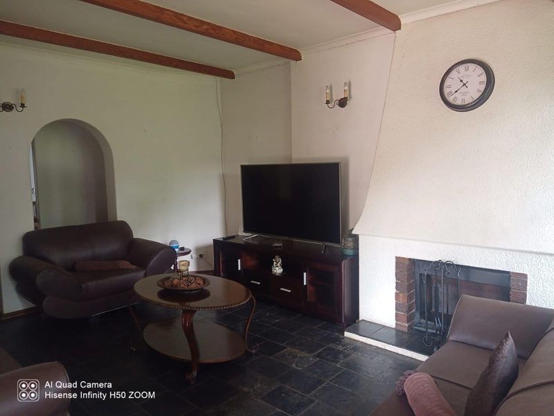 Living room featuring exposed timber ceiling beams, a traditional masonry fireplace, and dark slate tile flooring with an arched entryway.