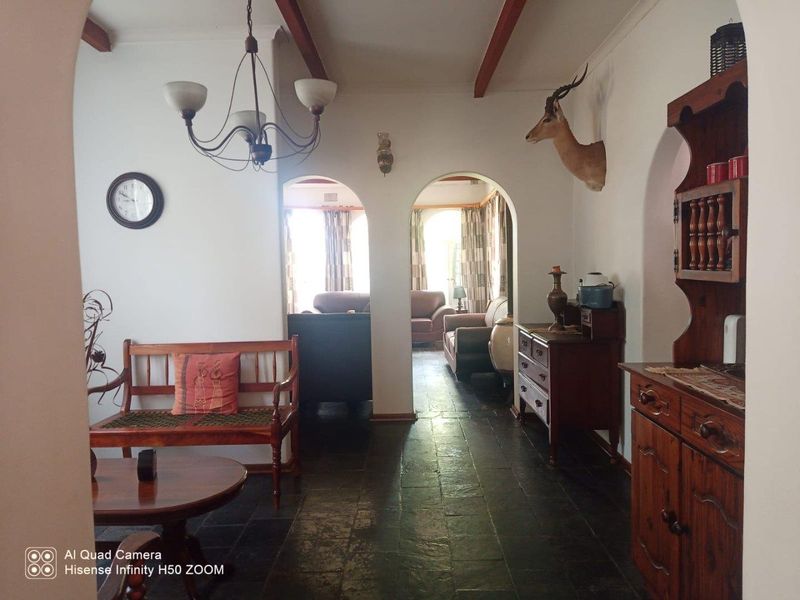 A living area featuring traditional arched doorways, exposed timber ceiling beams, and dark stone tile flooring, leading into an adjacent lounge space.