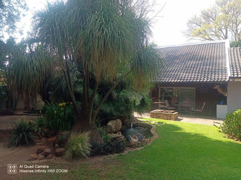Rear garden view featuring a paved patio, established trees, a small pond with a water feature, and brick exterior wall with sliding doors.