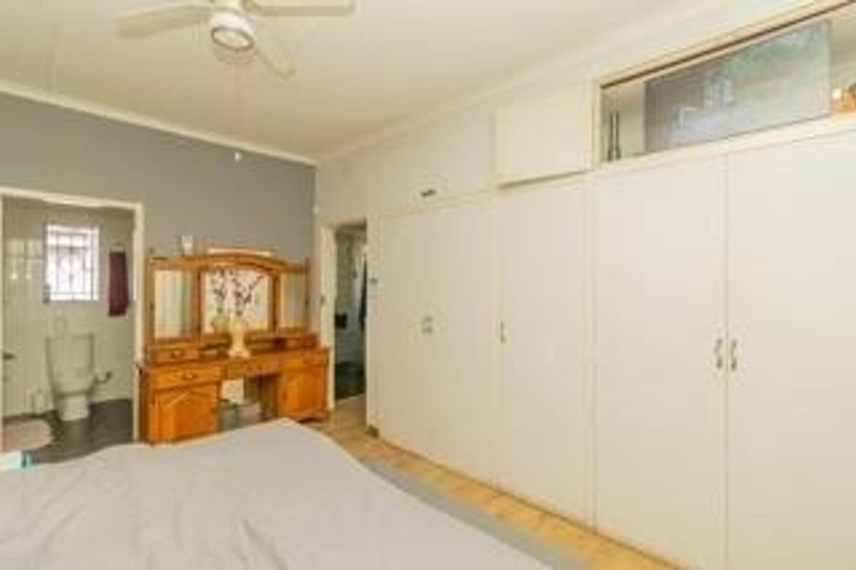Spacious bedroom featuring extensive built-in cupboards, a ceiling fan, and a transom window, with an adjoining en-suite bathroom visible.