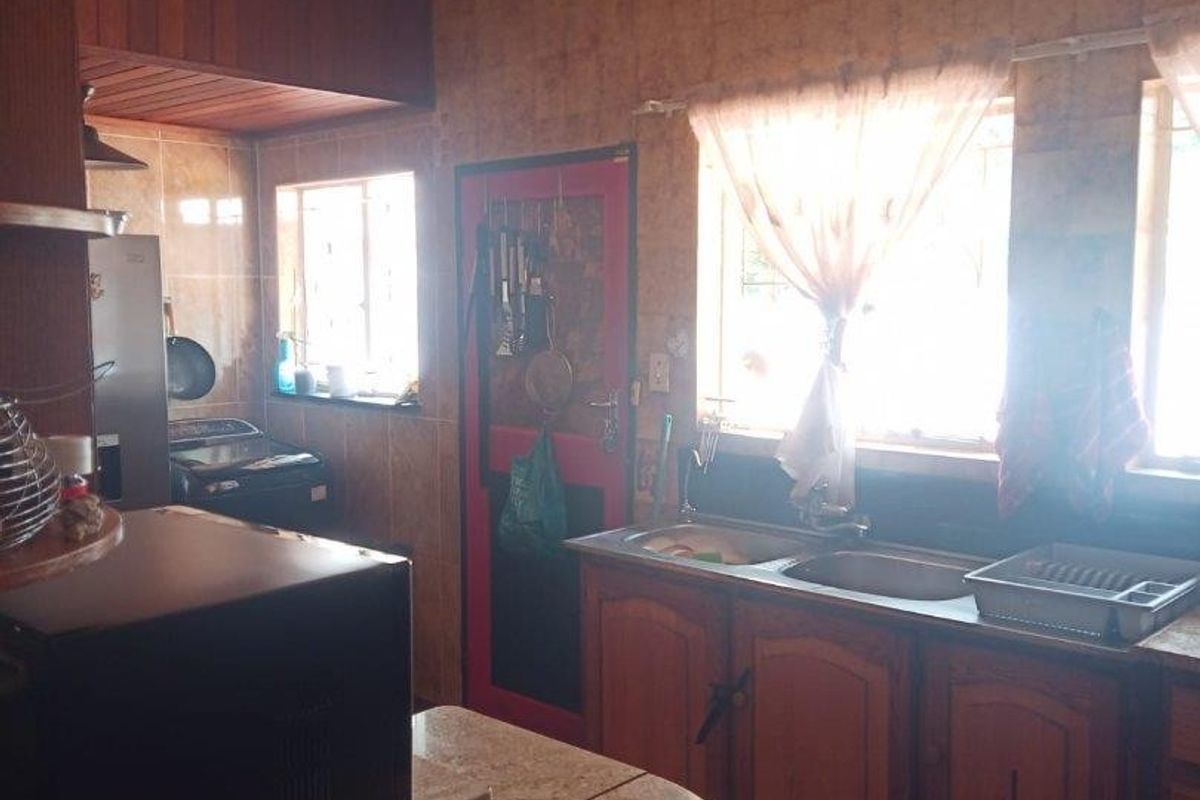 A dated kitchen featuring wooden cabinetry, a double basin sink, and tiled splashbacks, offering potential for a modern renovation.