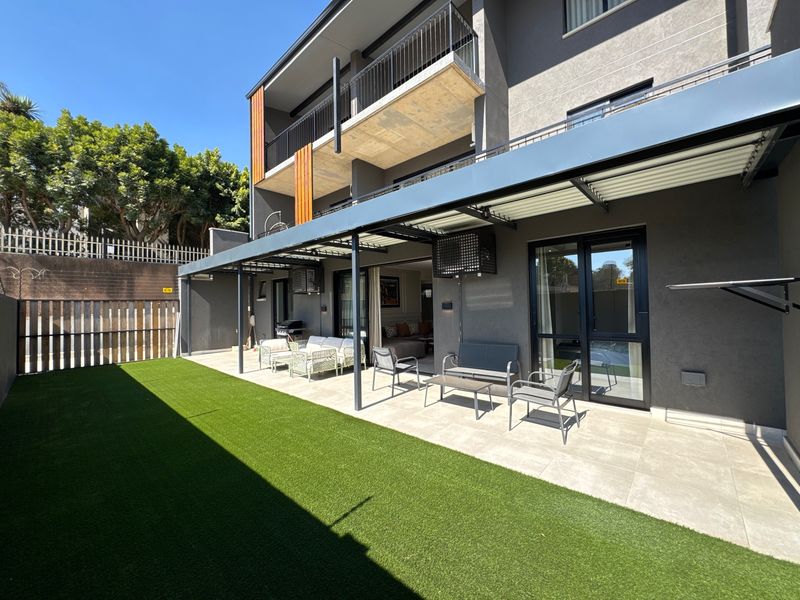 Modern ground floor apartment featuring a covered patio area, tiled flooring, and a private artificial lawn garden space.