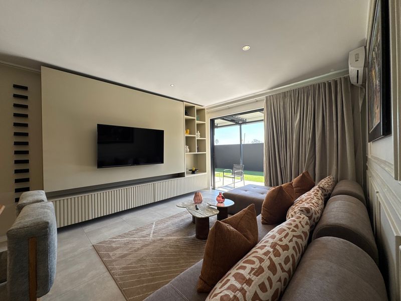 Modern living room featuring a custom built-in media wall with integrated shelving, tiled floors, and direct access to an outdoor patio area.