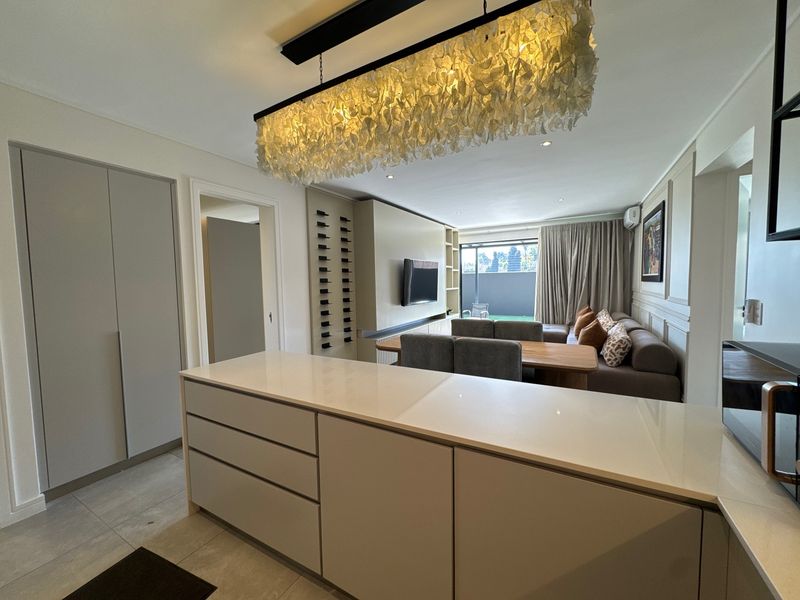 Modern open-plan living area featuring a sleek kitchen island with stone countertops, custom cabinetry, built-in wine storage, and elegant feature lighting.