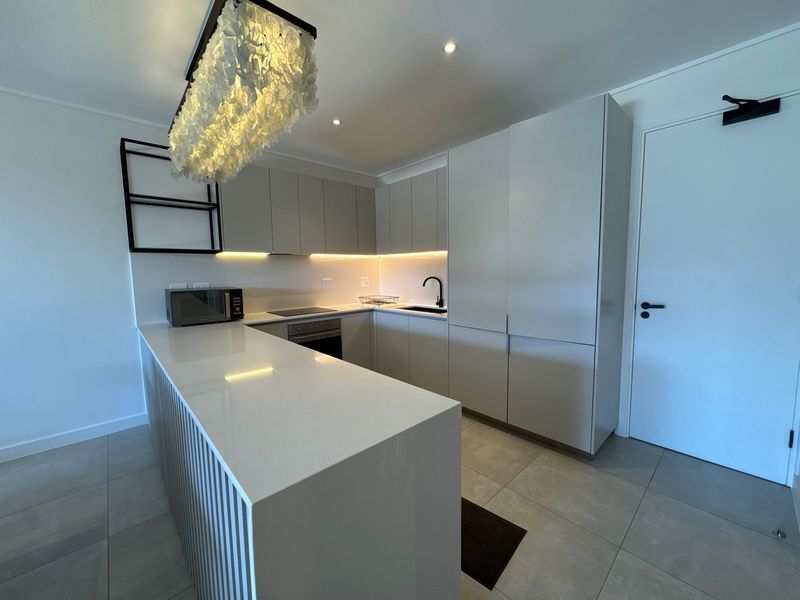 Modern kitchen featuring sleek handleless cabinetry, stone countertops, integrated appliances, and ambient under-cabinet lighting with a clean, minimalist aesthetic.