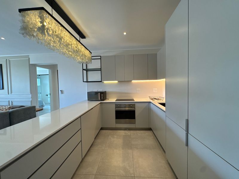 Modern kitchen featuring sleek handleless cabinetry, quartz countertops, integrated appliances, and stylish under-cabinet lighting, seamlessly flowing into the living area.