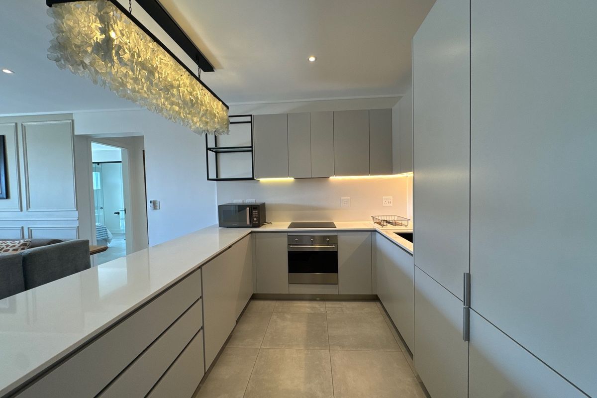 Modern kitchen featuring sleek handleless cabinetry, quartz countertops, integrated appliances, and stylish under-cabinet lighting, seamlessly flowing into the living area.