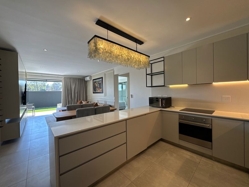 Modern open-plan kitchen and living area featuring sleek cabinetry, integrated appliances, stone countertops, and seamless access to an outdoor patio space.