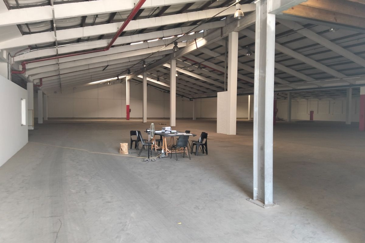 Expansive industrial warehouse space featuring high ceilings, exposed steel structural elements, concrete flooring, and an integrated fire sprinkler system.