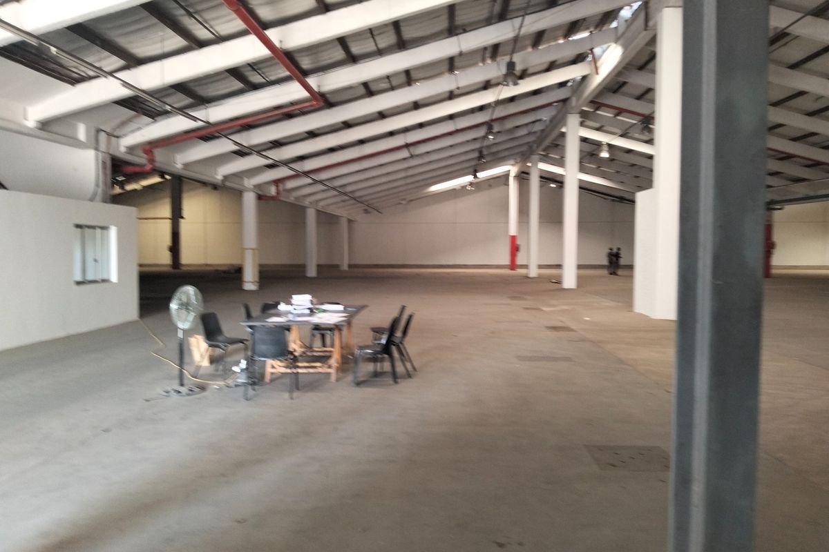 A large, open-plan industrial warehouse space featuring high ceilings with exposed steel trusses, concrete flooring, and functional fire sprinkler systems.