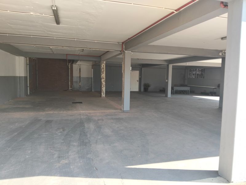 Spacious industrial garage area featuring exposed structural steel beams, concrete flooring, and functional overhead lighting, suitable for storage or workshop use.