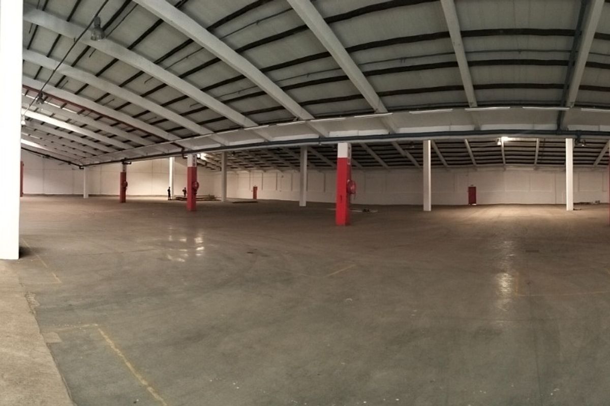 Expansive industrial warehouse space featuring high ceilings with exposed steel trusses, concrete flooring, and a mezzanine access staircase, suitable for storage or manufacturing.