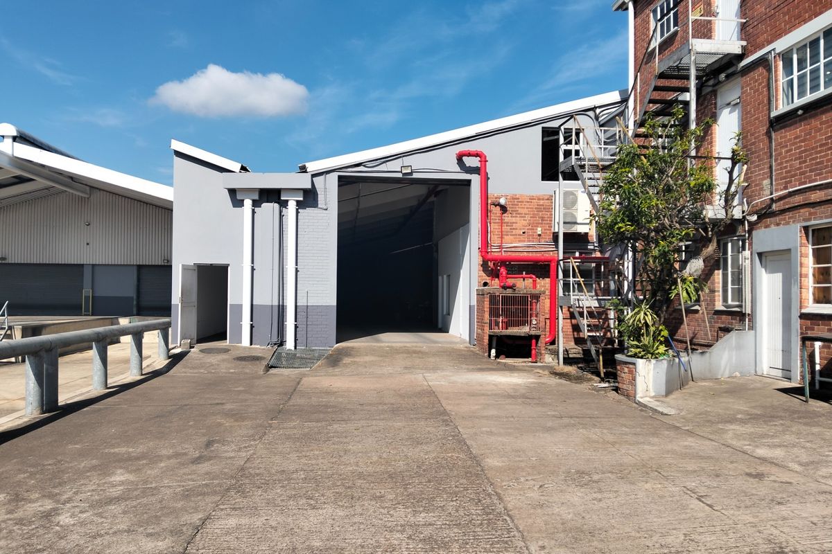 Rear industrial yard featuring a concrete driveway, external metal staircase, and exposed fire suppression piping on a brick and painted masonry building.