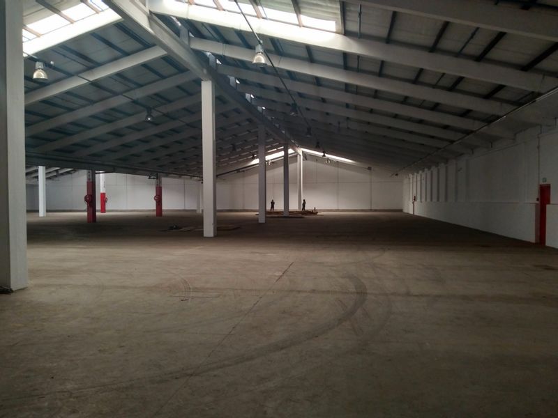 Expansive industrial warehouse space featuring high ceilings with exposed steel trusses, natural light from skylights, and durable concrete flooring.