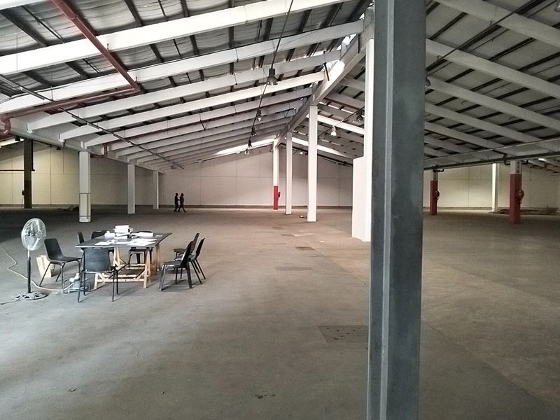 Large open-plan industrial warehouse space featuring high ceilings with exposed steel trusses, concrete flooring, and structural support columns.