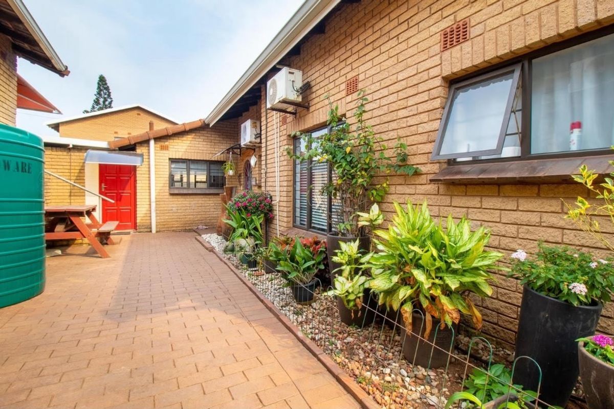 A well-maintained rear exterior area featuring a face brick facade, paved patio space, and a functional water storage tank.