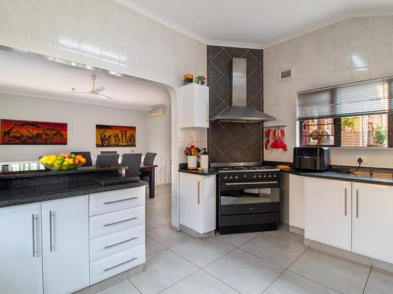 Open-plan kitchen featuring granite countertops, white cabinetry, and a stainless steel extractor fan, flowing into an adjacent dining area.