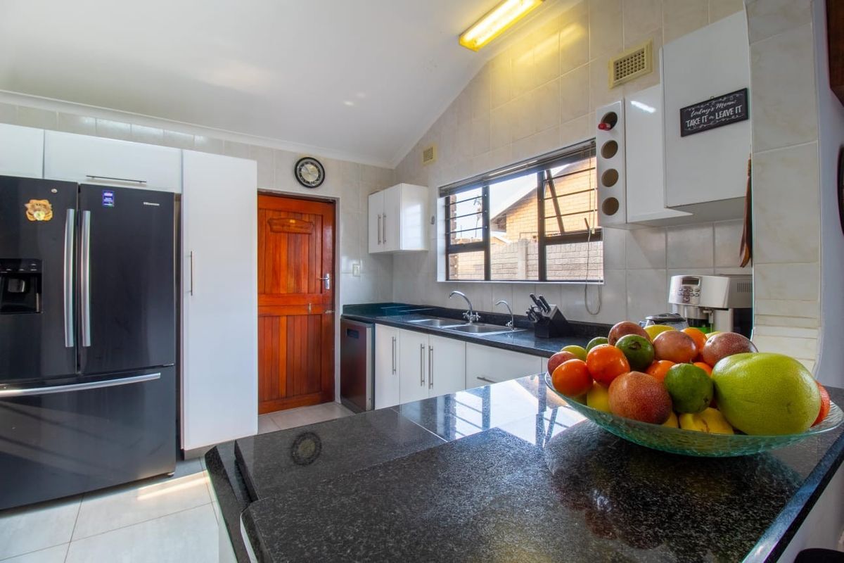 A functional kitchen featuring dark granite countertops, white cabinetry, a double sink, and tiled splashbacks with natural light from the window.