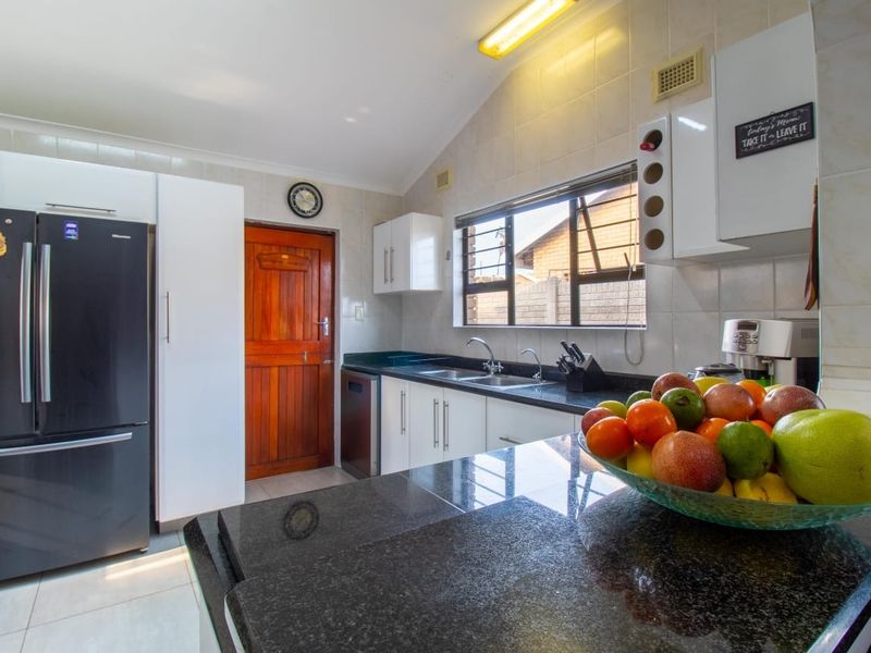 A functional kitchen featuring dark granite countertops, white cabinetry, a double sink, and tiled splashbacks with natural light from the window.