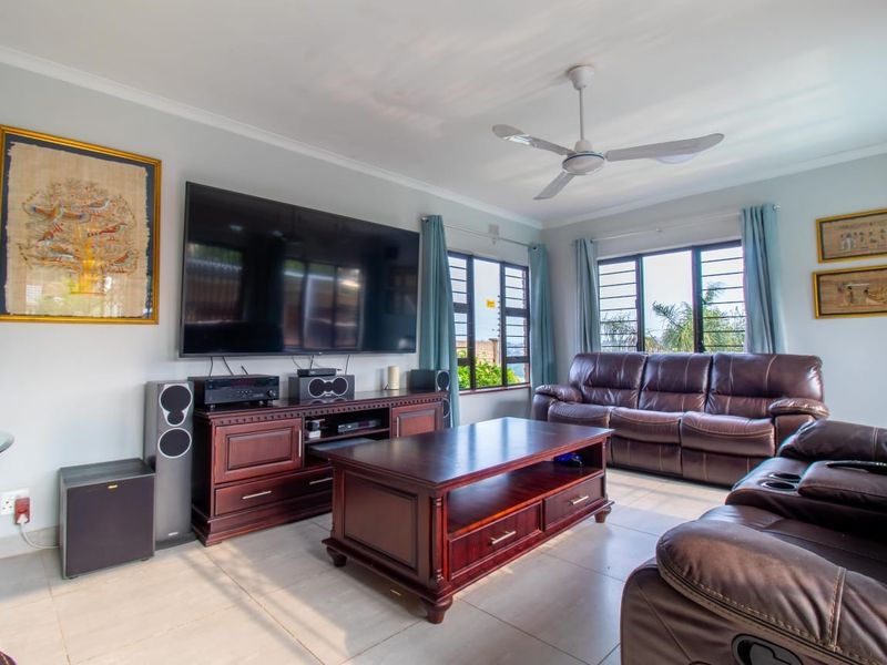A well-maintained living room featuring neutral tiled flooring, a ceiling fan, and large windows that provide ample natural light.