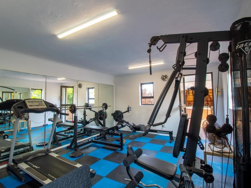 Dedicated home gym space featuring wall-to-wall mirrors, durable rubber flooring, and bright overhead lighting, providing a functional area for fitness activities.