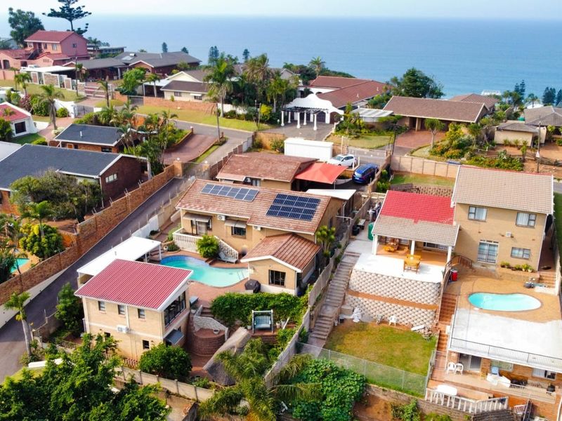 Aerial view of a coastal residential neighborhood featuring multiple homes with swimming pools, tiled roofs, and solar panel installations.