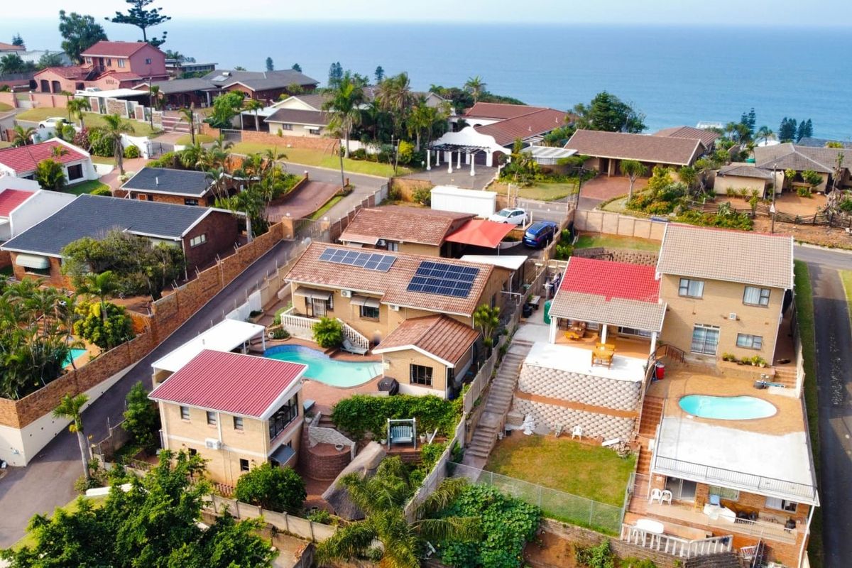 Aerial view of a coastal residential neighborhood featuring multiple homes with swimming pools, tiled roofs, and solar panel installations.