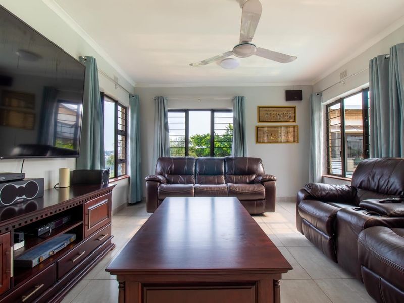 A well-lit living room featuring tiled flooring, a ceiling fan, and large windows with security bars, providing a comfortable and functional space.