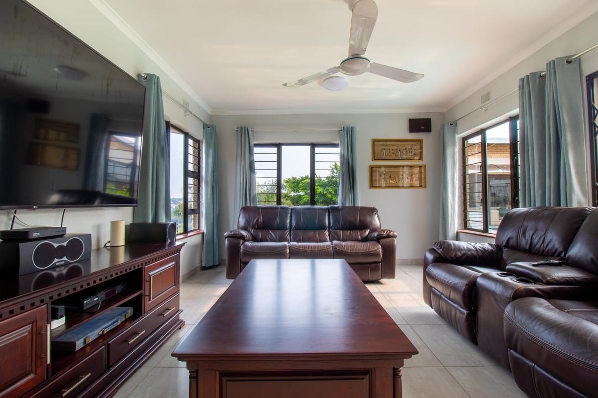 A well-lit living room featuring tiled flooring, a ceiling fan, and large windows with security bars, providing a comfortable and functional space.