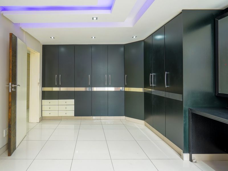 Spacious bedroom featuring extensive built-in dark cabinetry, modern recessed ceiling lighting with cove accents, and clean tiled flooring throughout.