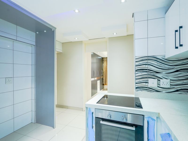 Modern kitchen featuring built-in oven, electric hob, quartz countertops, and contemporary tiled backsplash with ample storage cabinetry.