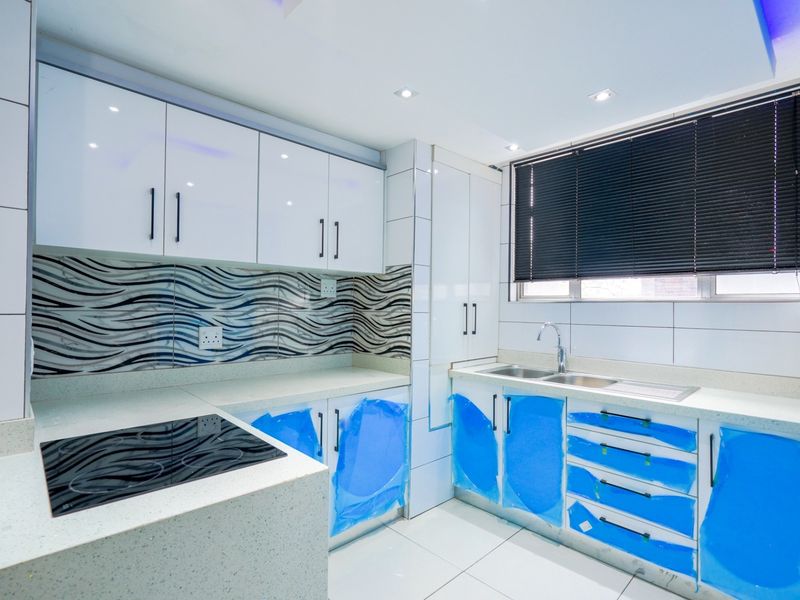 Modern kitchen featuring high-gloss white cabinetry, stone countertops, integrated electric hob, and a double sink with contemporary tiled backsplash.
