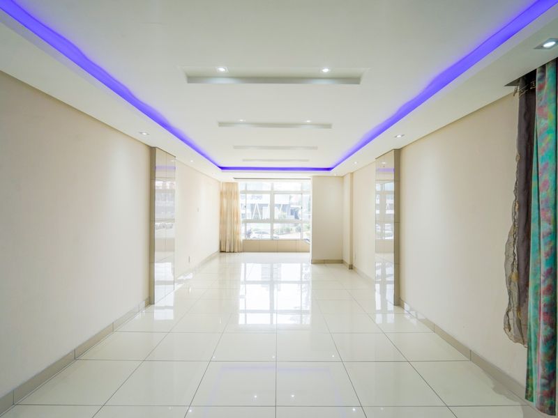 A bright, spacious, and empty living area featuring polished tiled floors, modern recessed ceiling lighting, and decorative LED strip accents.