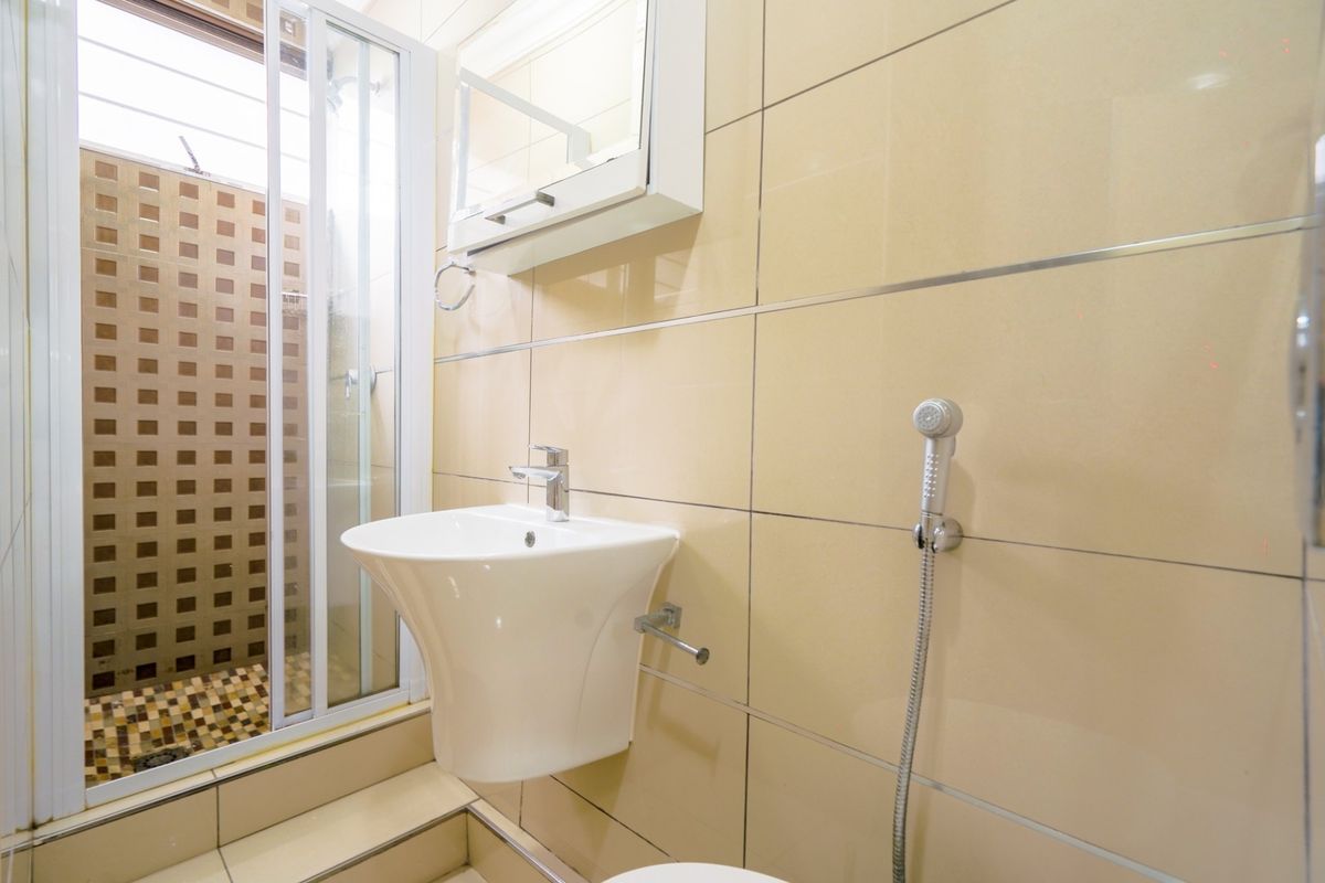 A functional bathroom featuring a wall-mounted basin, a shower enclosure with tiled accents, and a built-in medicine cabinet.