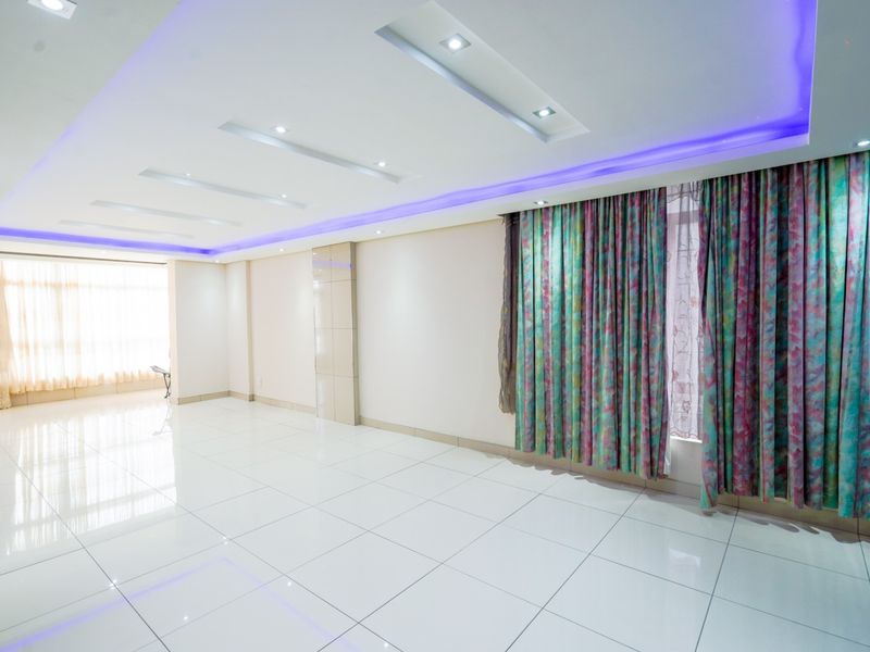 Spacious, empty living area featuring polished tiled flooring, recessed ceiling lighting with integrated LED accents, and large windows with installed curtain tracks.