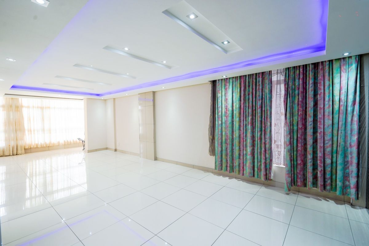 Spacious, empty living area featuring polished tiled flooring, recessed ceiling lighting with integrated LED accents, and large windows with installed curtain tracks.