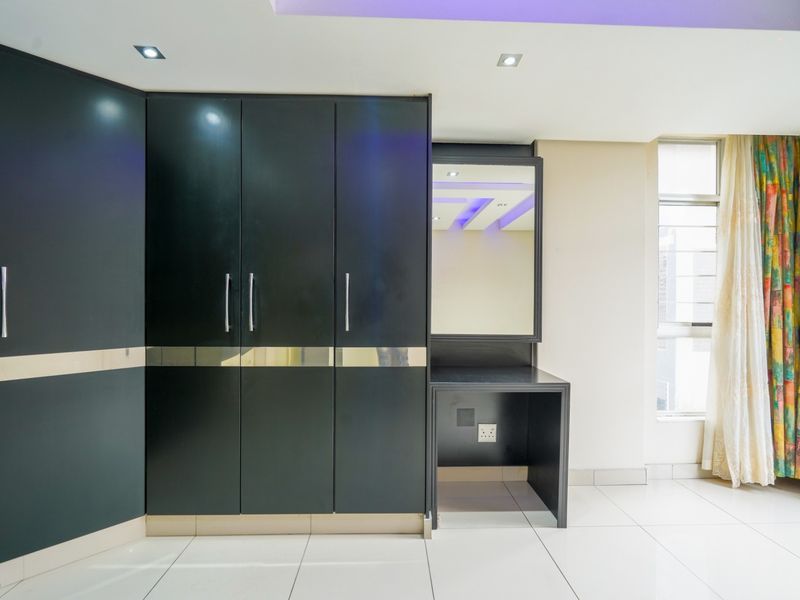 A bright bedroom featuring modern black built-in cupboards with an integrated vanity, tiled flooring, and recessed ceiling lighting.
