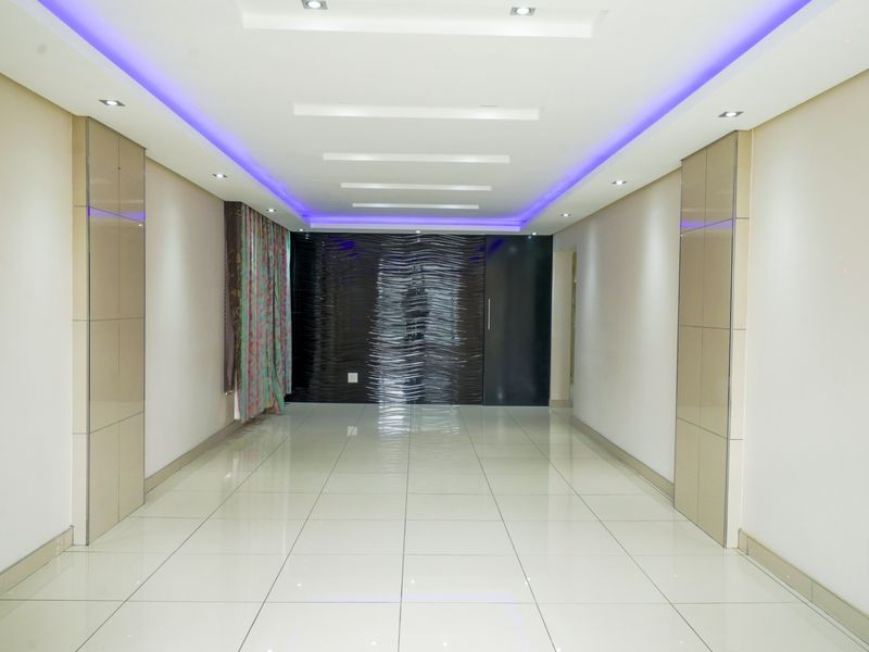 A spacious, empty living area featuring polished tiled floors, modern recessed ceiling lighting with purple LED accents, and a textured feature wall.