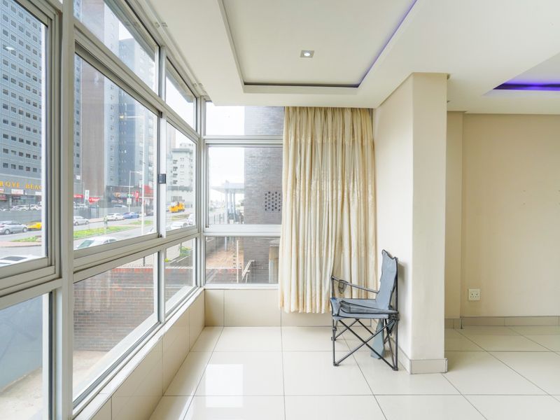 Bright and spacious living area featuring large floor-to-ceiling windows with urban views, tiled flooring, and modern recessed ceiling lighting.