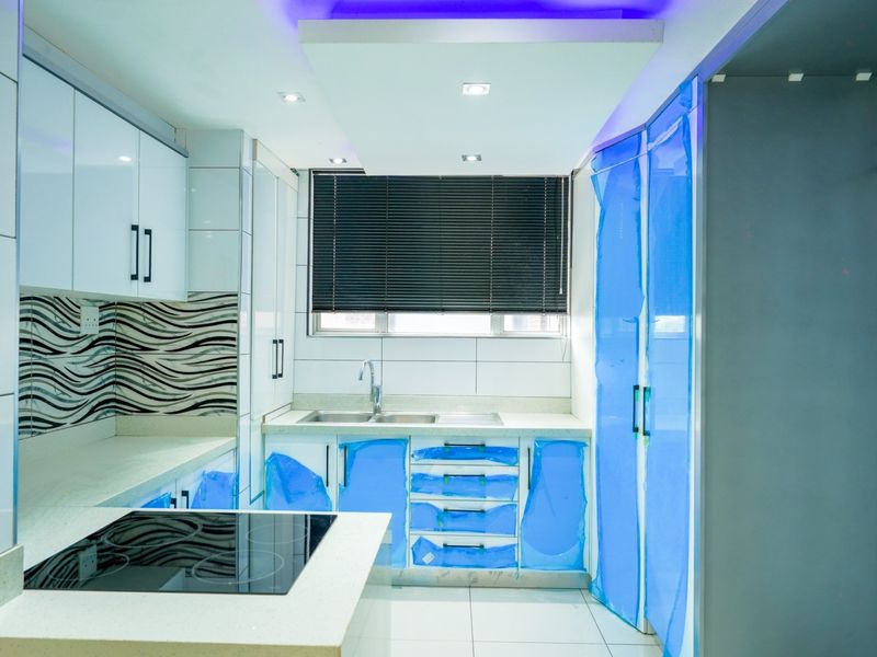 Modern kitchen featuring white high-gloss cabinetry, stone countertops, integrated electric hob, and recessed lighting. The space appears newly installed and ready for use.